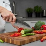 Monarch Cutlery Santoku Cleaver Chef Knife slicing fresh vegetables and meat on a wooden cutting board.
